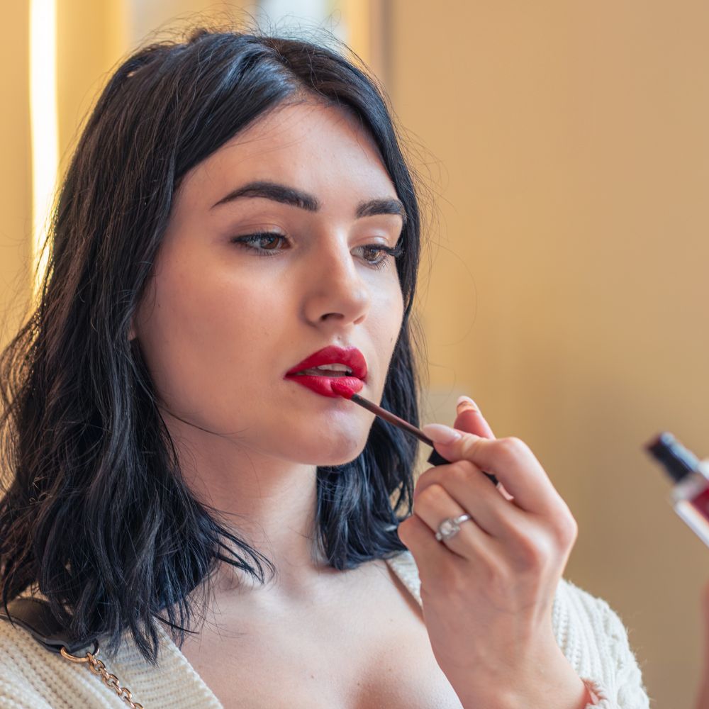 Beautiful woman applying bold red lipstick with a makeup brush